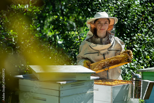 Young female beekeeper hold wooden frame with honeycomb. Collect honey. Beekeeper on apiary. Beekeeping concept.