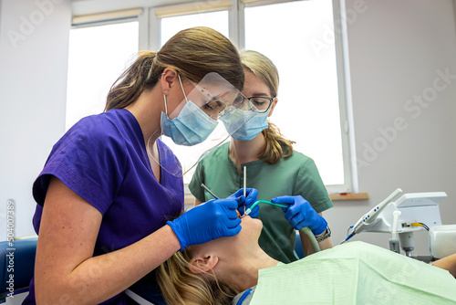 Pretty female patient sitting in armchair while doctor with assistant examining her teeth