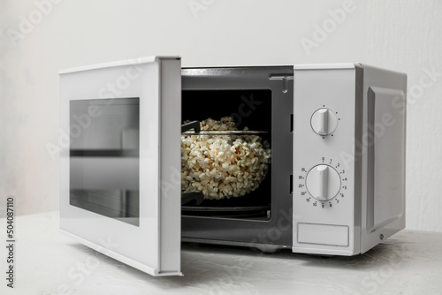 Bowl with popcorn in microwave oven on light background