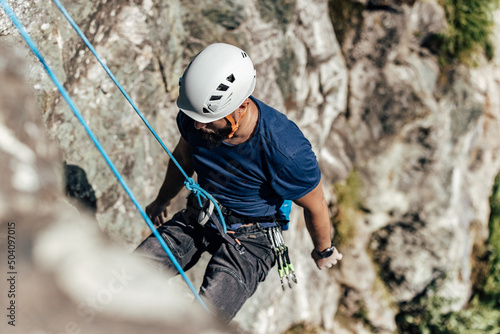 An adult man belays down a rock face after reaching the top.
