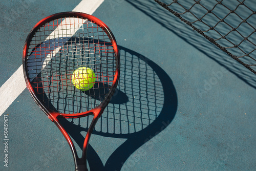 Overhead view of red tennis racket on ball and court with line during sunny day