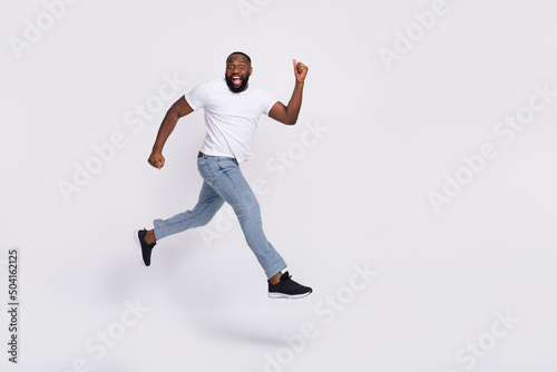 Photo of excited pretty guy dressed casual t-shirt jumping high running hurry isolated white color background