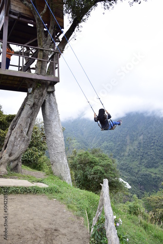 Tourist having fun swinging on Giant Swing. View of green mountains and trees in background. Banos