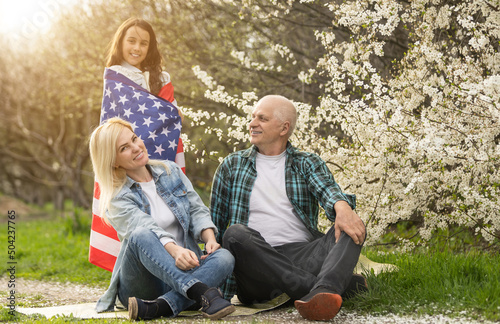 Portrait of happy family celebrating 4th July Independence Day holding silhouette usa national flag against park
