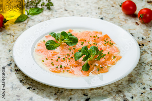 Salmon carpaccio on a white plate on marble table