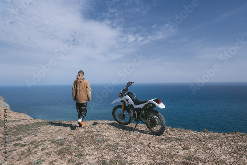 Woman relaxing with dirtbike on the top of mountain with stunning sea views