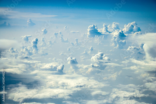 Cloudscape with abstract strange towering cumulus (congestus) cloud figures above the cirrus clouds and dark blue sky taken from plane window