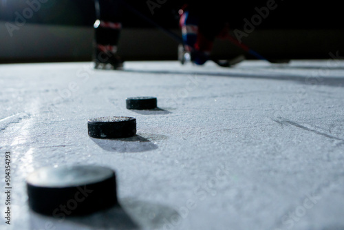 Black hockey pucks on the ice rink of the stadium. Athlete training in hockey on a dark ice arena, sports school. Winter sports competition. Puck on ice powdered with snow close up.