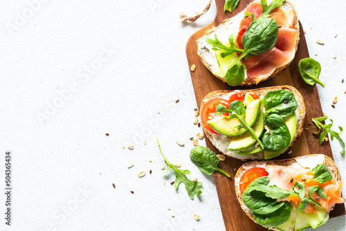 Open sandwich set with cream cheese, prosciutto, salmon, avocado and fresh greens. Top view at white table. Close up.