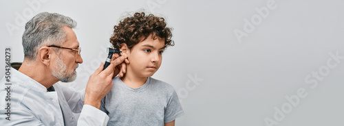 Positive curly male child while ear examining with audiologist. ENT doctor checking boy ear using otoscope