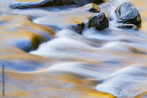 Landscape of the Little River captured with motion blur and aglow with reflected color from sunlit autumn foliage, Great Smoky Mountains National Park, Tennessee, USA