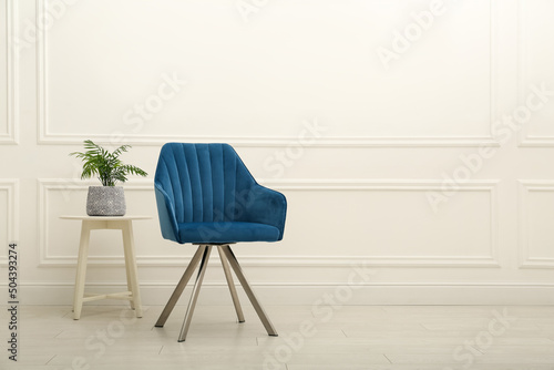 Modern blue armchair and houseplant on wooden table near white wall indoors. Space for text