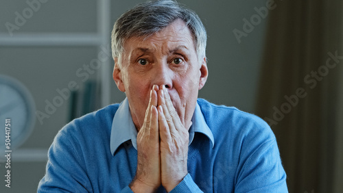 Depressed frustrated old senior Caucasian man shocked sad elderly mature 60s male feeling worried looking at camera cover mouth holding head stressed businessman expression indoor health trouble