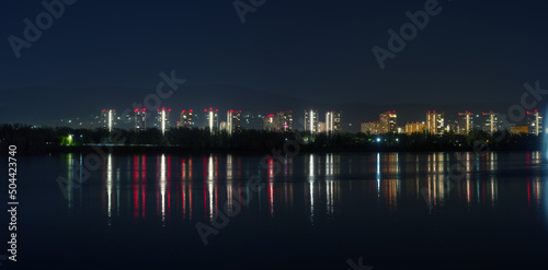 Panorama of the night city. Houses are reflected in the water. Siberian city of Krasnoyarsk