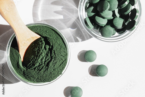 natural additives and superfood. green spirulina algae powder and pills in glass bowls on white background. healthy lifestyle concept. organic food