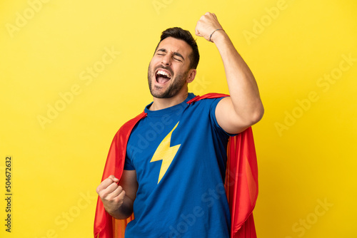 Young handsome caucasian man isolated on yellow background in superhero costume and celebrating a victory