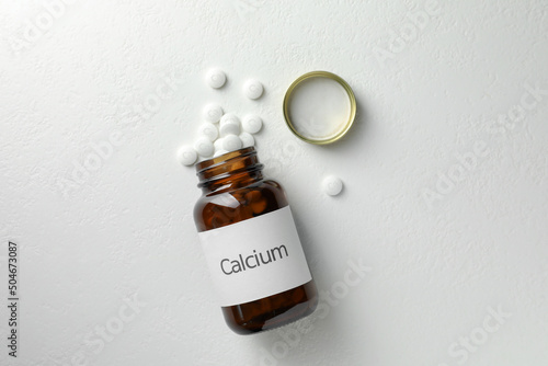 Overturned bottle of calcium supplement pills on white table, flat lay