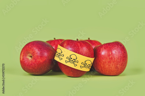 Apples with poison skull symbol sticker on green background. Concept of pesticide residues in agricultural food