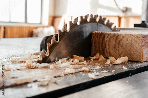 The blade of a circular saw on the desktop cuts a pine board.