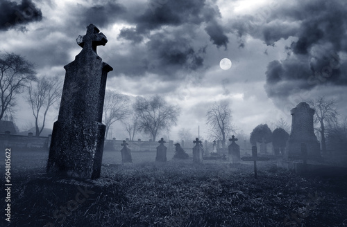 Old creepy graveyard on stormy winter day with full moon in black and white