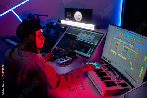 Beautiful caucasian girl in stylish clothes works in a recording studio with neon light in a cap and glasses