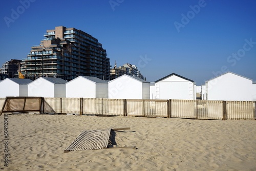 Traditionelle weiße Strandkabinen und moderne Hochhaus Architektur am Strand der Nordsee bei blauem Himmel und Sonnenschein in Knokke-Heist bei Brügge in Westflandern in Belgien