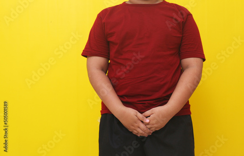 Asian boy standing with holding pee gesture. Isolated on yellow background.