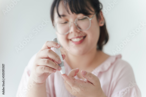 Asian woman using lancet on finger for checking blood sugar level by Glucose meter, Healthcare and Medical, diabetes, glycemia concept