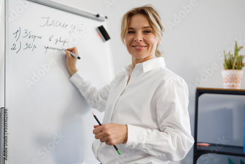 Smiling business woman in formal wear writes on flipchart during presentation or lecture in office.