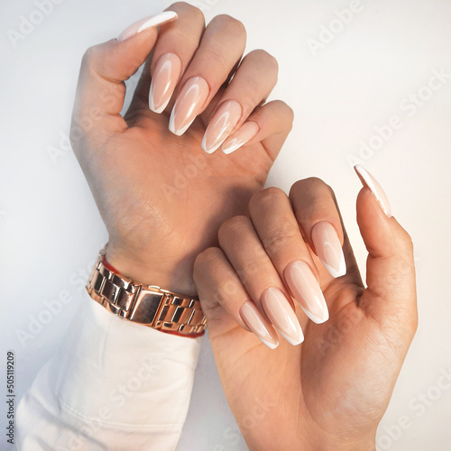 Gentle camouflage gel polish on long square nails with a French design. Hands with a professional manicure in a shirt. Trendy nail extension with French design.