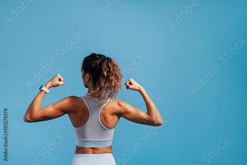 Rear view of young woman showing her biceps on blue background with a lot of copy space