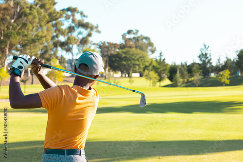 Rear view of african american young man wearing cap playing golf against clear sky at golf course