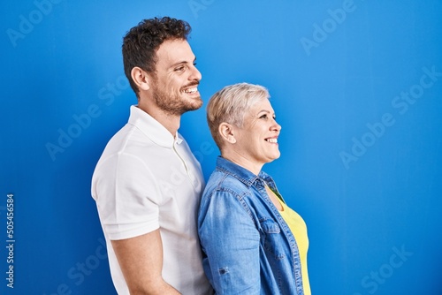 Young brazilian mother and son standing over blue background looking to side, relax profile pose with natural face and confident smile.