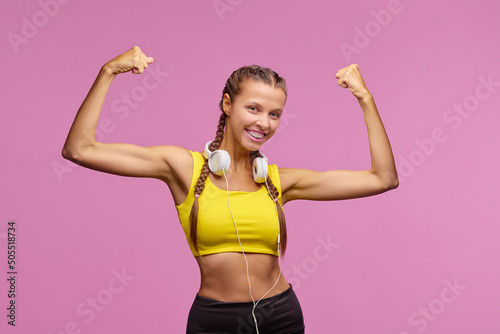 Healthy lifestyle. Happy young woman showing her muscle strong arms. Studio shot. Pink background.