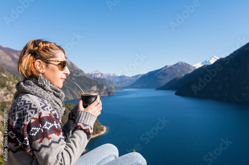  Between landscapes of lakes and mountains, a beautiful woman relaxes with a mate. National drink of Argentina.