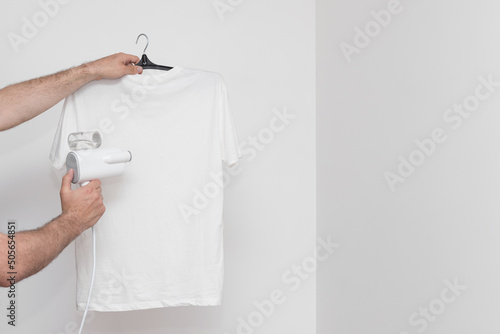 Steam the T-shirt with a portable steamer on a white background. copyspace