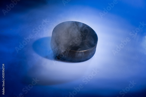 Closeup of a rubbery ice hockey puck against a blue smoky background.