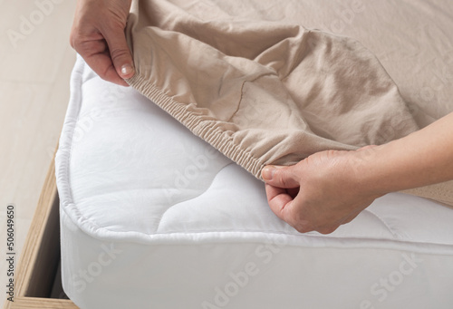 Woman puts beige sheets on the bed. Sheet on elastic band top view