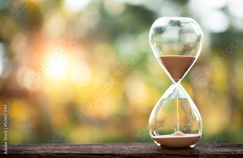 hourglass (sand clock) on an old wooden table with a natural blur background, Hourglass as time passing concept for business deadline, Life-time passing concept, elapsed time concept, copy space