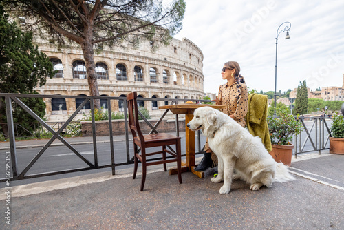 Woman sitting with her dog at outdoor cafe near coliseum, the most famous landmark in Rome. Concept of italian lifestyle with pets and traveling Italy