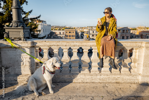 Woman enjoys beautiful cityscape of old Rome city, standing back with her dog on the top of Spanish steps in the morning. Concept of italian lifestyle and travel
