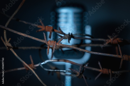 Microphone behind barbed wire as a symbol of discrimination, free speech crisis, political persecution and repression. Selective focus on barbed wire. Horizontal image.