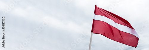 Latvian flag waving in wind. Flag of Latvia on cloudy white sky background. 