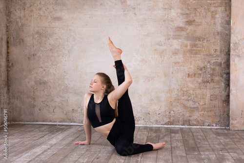 Young girl teenager doing stretching in gym. Blond woman gymnast ballerina in black sportswear dancing. Girl doing acrobatic figures and string. Girl standing on hands