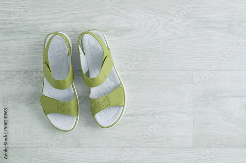 Green women's sandals on wooden white floor. View from above.