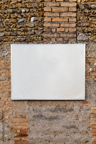Cartello rettangolare bianco appeso al vecchio muro di mattoni e pietra. Fotografia verticale.