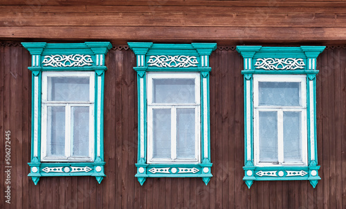 Three old windows with wooden turquoise architraves with patterns on brown board wall.