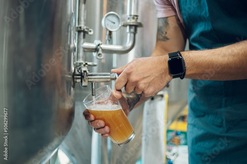 Close shot of a man filling glass of beer on a tap in brewery