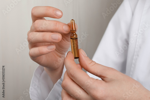 Woman holding pharmaceutical ampoule with medication on white background, closeup