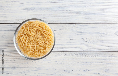 Uncooked vermicelli pasta in glass bowl on white wooden table